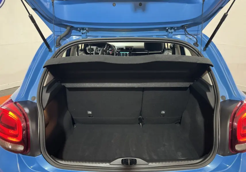 Vue arrière du coffre ouvert d'une Citroën C3 bleu 2018, montrant l'intérieur spacieux et la tablette de coffre relevée.