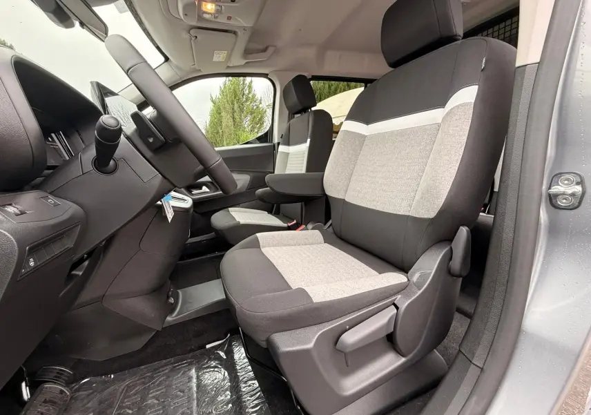 Vue intérieure côté conducteur du Citroën Berlingo gris Artense 2025, sièges tissu bicolore avec accoudoir central.