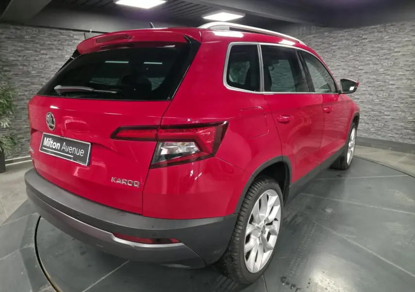 Vue 3/4 arrière droite d'un Skoda Karoq rouge avec jantes alliage argent et hayon fermé en intérieur showroom.