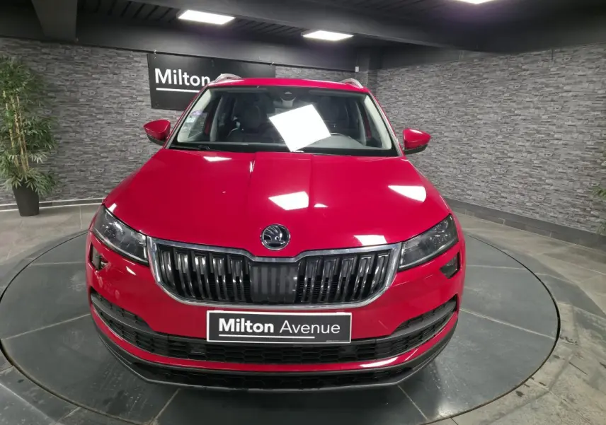 Vue frontale d'un Skoda Karoq rouge brillant avec calandre noire et plaque Milton Avenue en intérieur showroom.