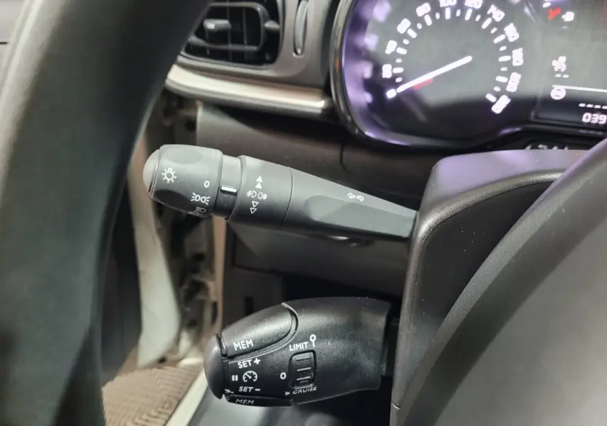 Gros plan sur les commandes au volant de la Citroën C3 beige, avec tableau de bord et indicateur de vitesse partiellement visibles.