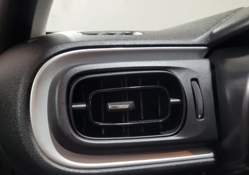 Gros plan sur la sortie d’air rectangulaire noire avec contour argenté du tableau de bord intérieur d’une Citroën C3 beige.