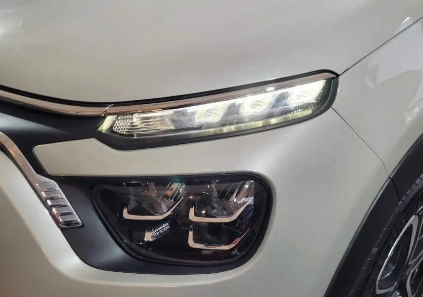 Gros plan sur le phare avant droit allumé d'une Citroën C3 beige 2022 avec signature lumineuse LED distinctive.