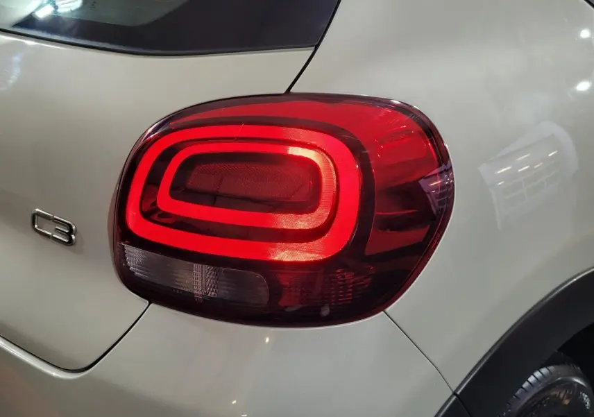 Feu arrière droit allumé sur une Citroën C3 beige vue de près, avec logo C3 visible sur la carrosserie.