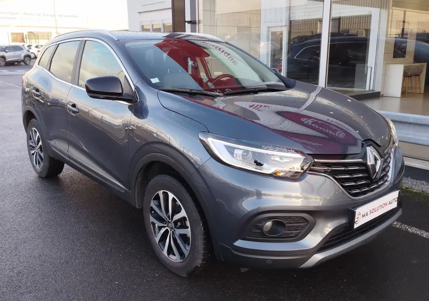 Renault Kadjar gris titanium en 3/4 avant droit, avec jantes bi-ton et calandre noire brillante.