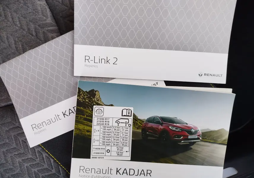 Vue 3/4 avant d’un Renault Kadjar rouge roulant sur une route de montagne sous un ciel clair.