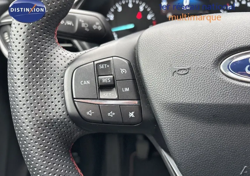 Gros plan sur le volant perforé avec commandes intégrées du Ford Puma gris Solar, tableau de bord flou en arrière-plan.