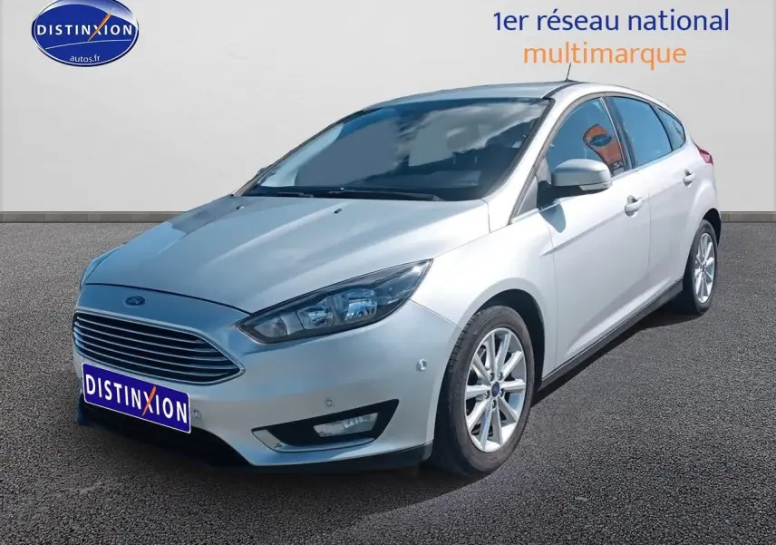 Ford Focus gris clair vue 3/4 avant droit sur parking avec calandre chromée et jantes alu