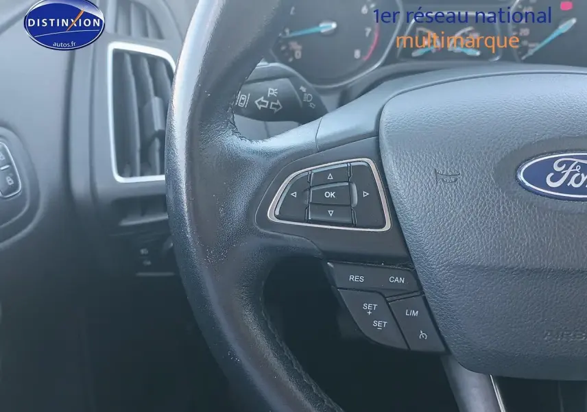 Gros plan sur le volant cuir multifonction de la Ford Focus gris clair, avec commandes au volant visibles côté gauche.