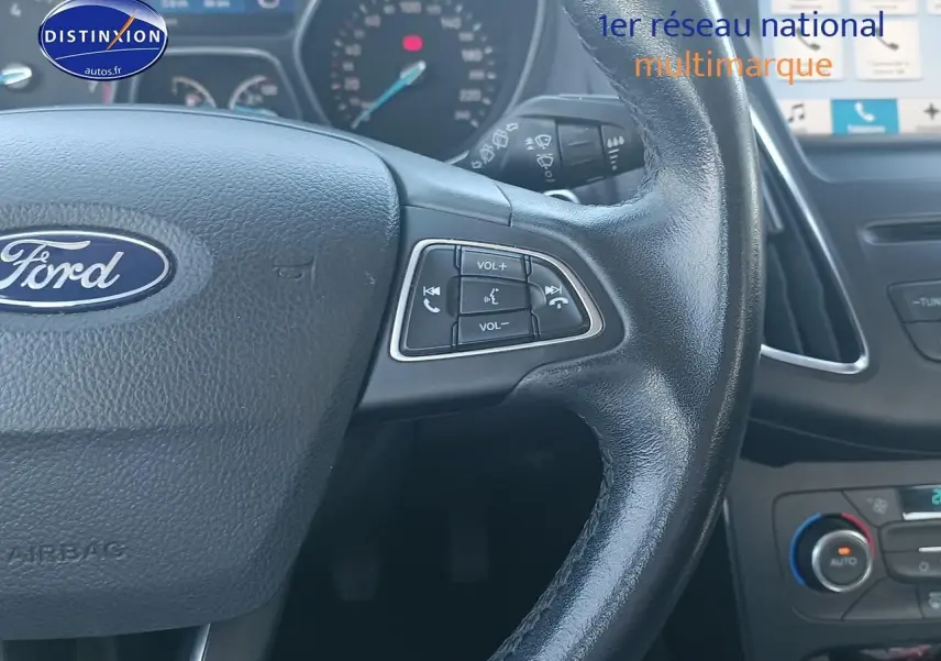 Gros plan sur le volant cuir multifonction d'une Ford Focus 2017, avec commandes audio et tableau de bord en arrière-plan.