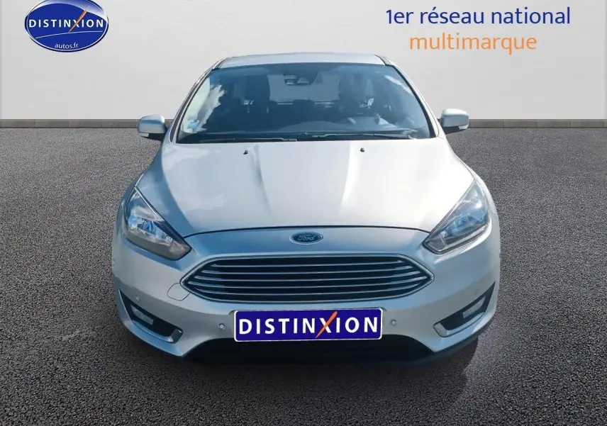 Vue avant d'une Ford Focus gris clair 2017 avec calandre chromée et phares halogènes allumés.