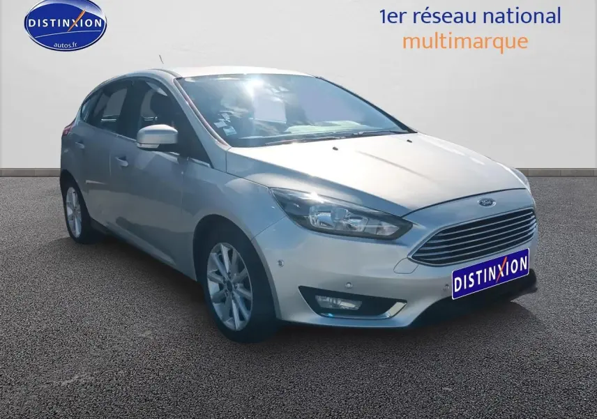 Ford Focus gris clair vue 3/4 avant droit avec calandre chromée et jantes alu sur fond neutre