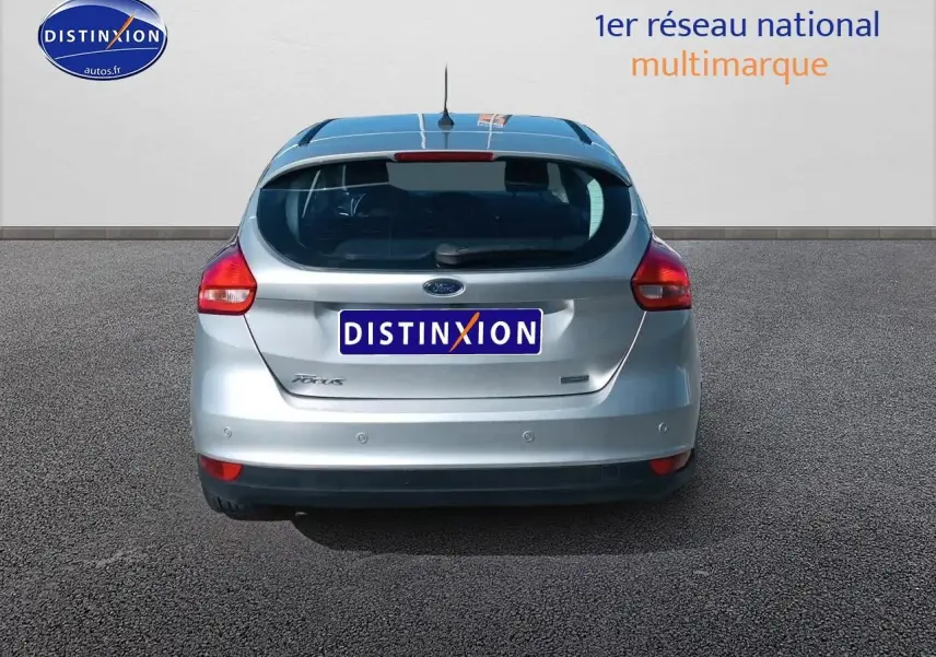 Vue arrière d'une Ford Focus gris clair 2017 avec feux rouges et logo Ford visible sur un sol goudronné.