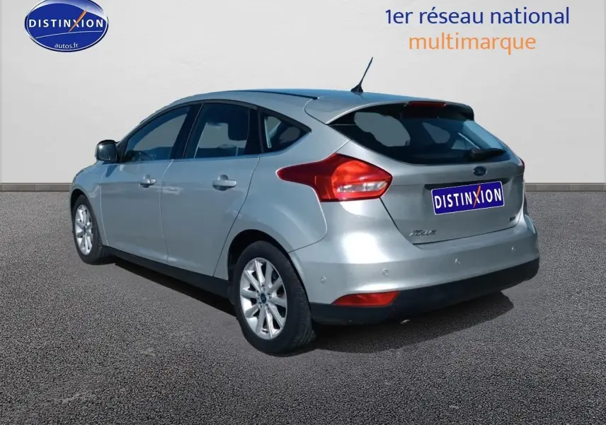 Ford Focus gris clair vue 3/4 arrière droit avec jantes alu et becquet arrière sur fond neutre.