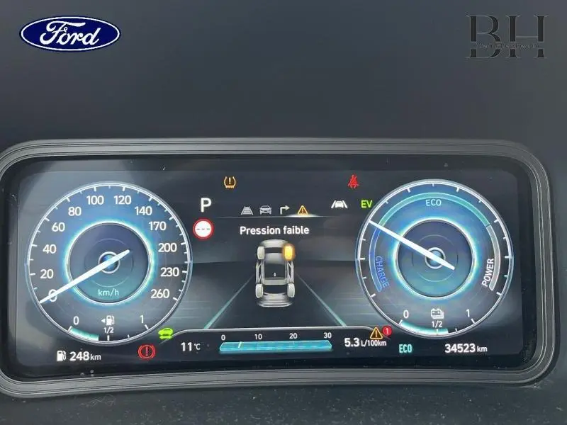 Tableau de bord numérique affichant une alerte de pression faible sur roue, avec compteurs vitesse et énergie.