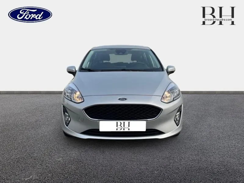 Vue avant d'une Ford Fiesta 1.1 75ch Cool & Connect gris lunaire avec calandre noire et phares allumés.