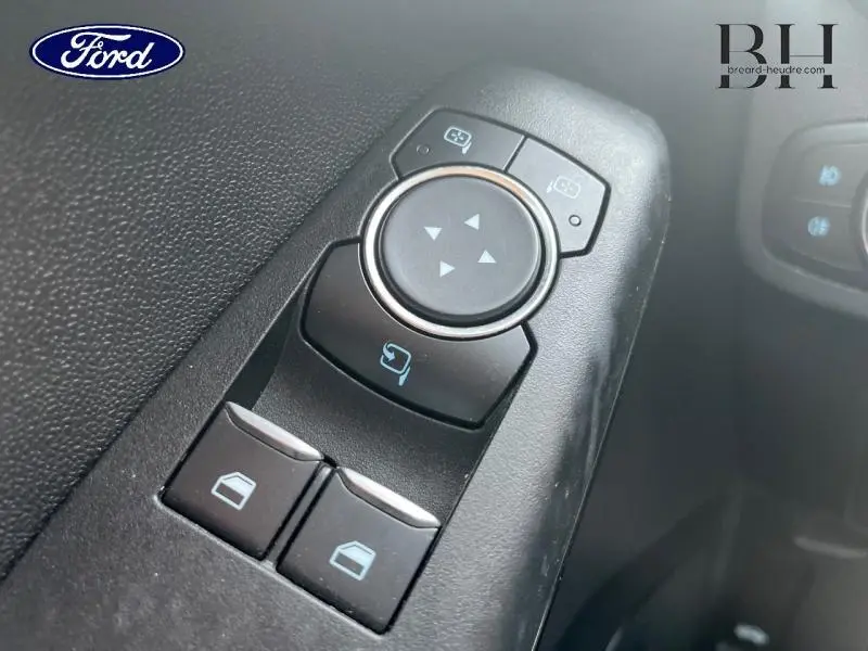 Gros plan sur les commandes de réglage des rétroviseurs et des vitres côté conducteur d'une Ford Fiesta gris lunaire.