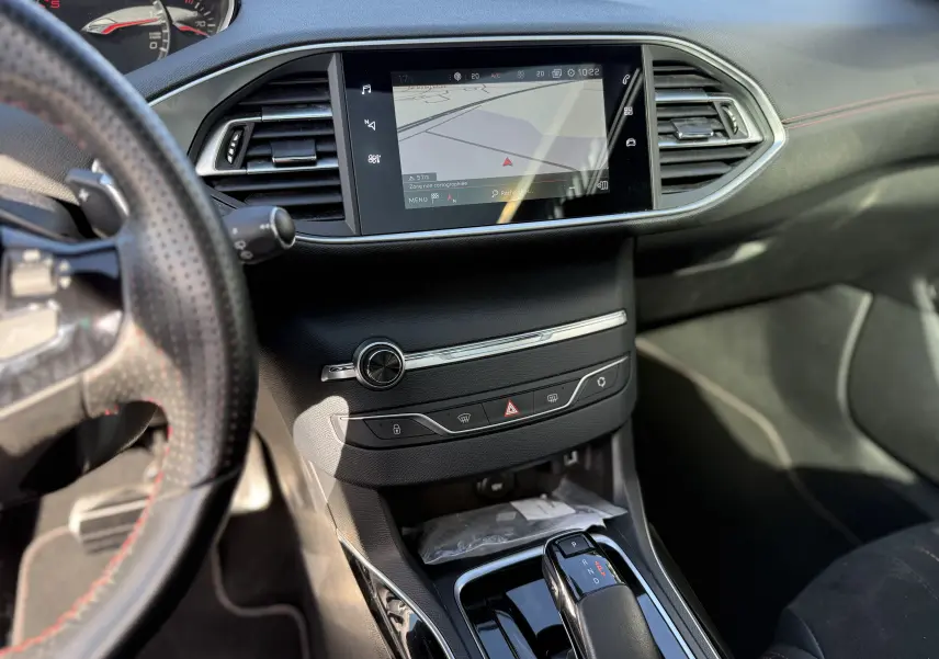 Vue intérieure centrée sur la console centrale et l’écran tactile de la Peugeot 308 SW, volant partiellement visible à gauche.