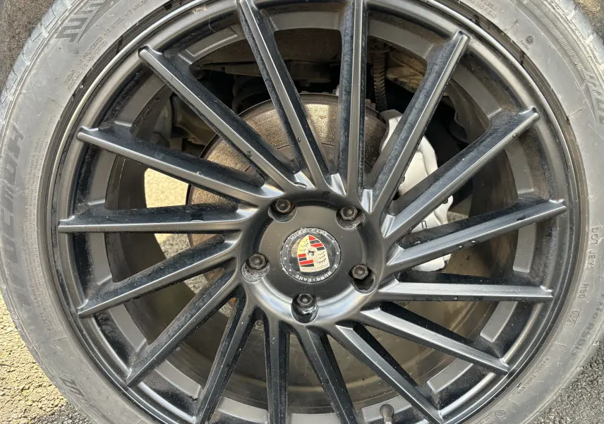 Gros plan sur la jante noire multi-branches d’un Porsche Cayenne S 4,8L V8 de 2007 avec logo Porsche au centre.