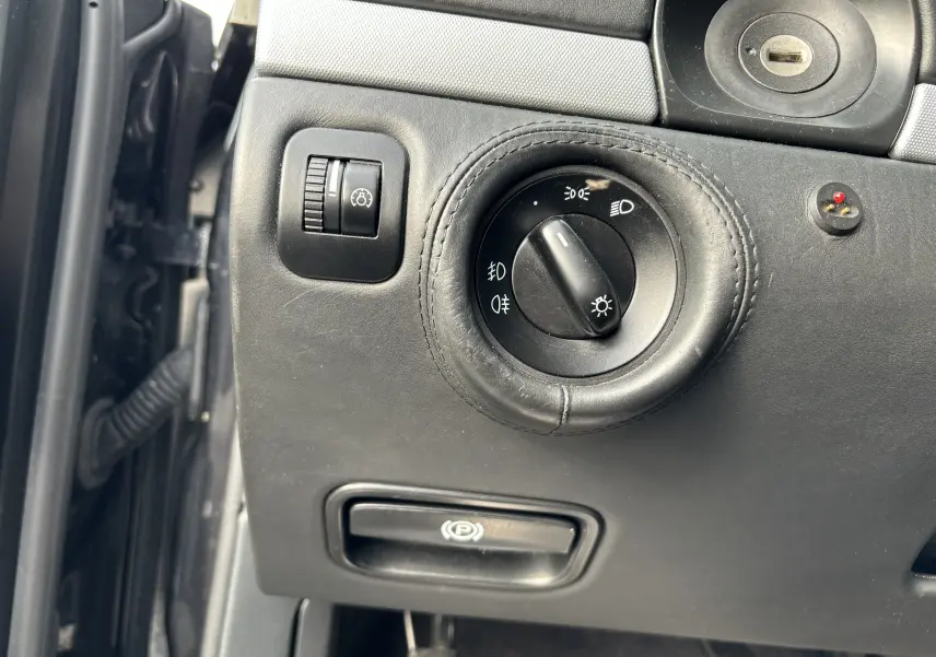 Gros plan sur le tableau de bord noir du Porsche Cayenne 2007, montrant la commande des phares et le frein à main électrique.