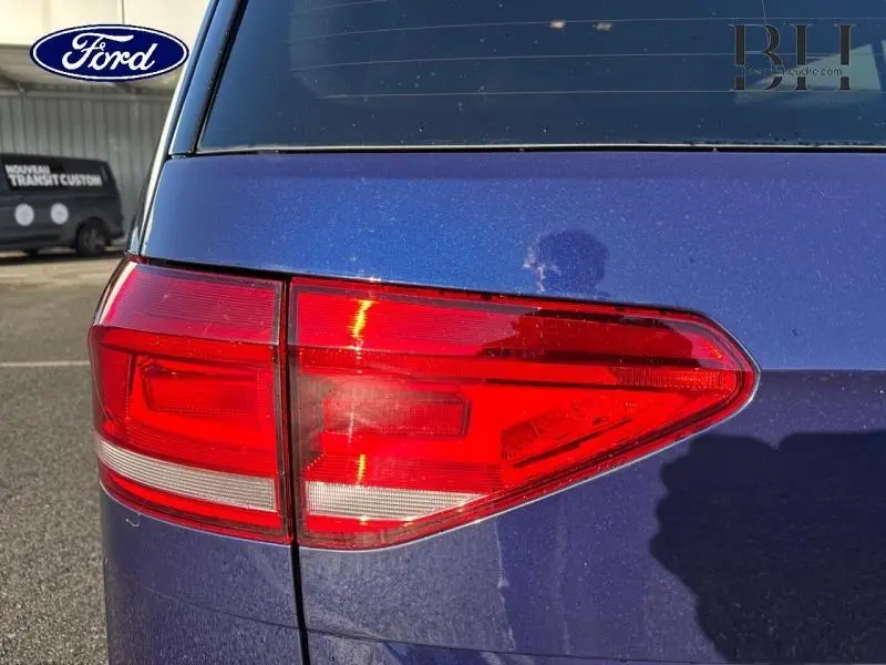 Gros plan sur le feu arrière droit d’un Volkswagen Touran bleu Atlantique métallisé, avec reflet et partie de la lunette arrière visible.