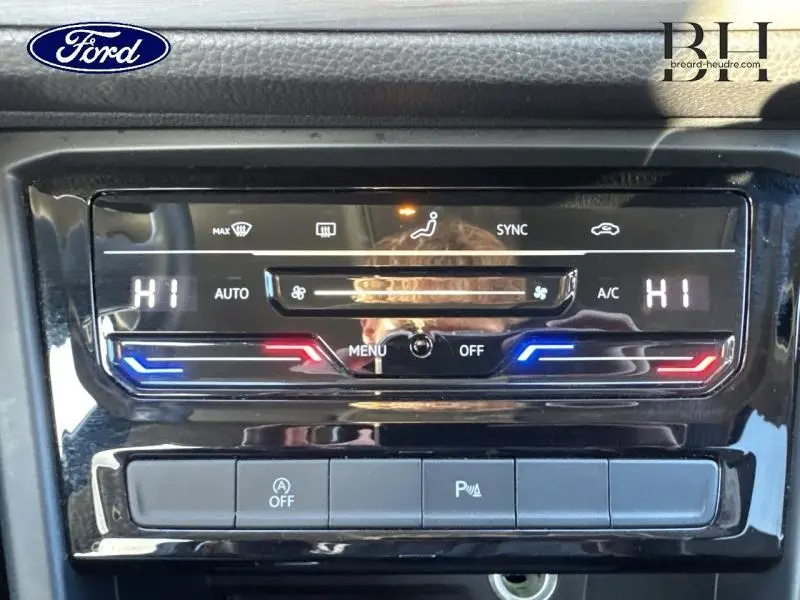 Panneau de commande de climatisation digitale avec réglages température et ventilation, sur tableau de bord noir brillant.