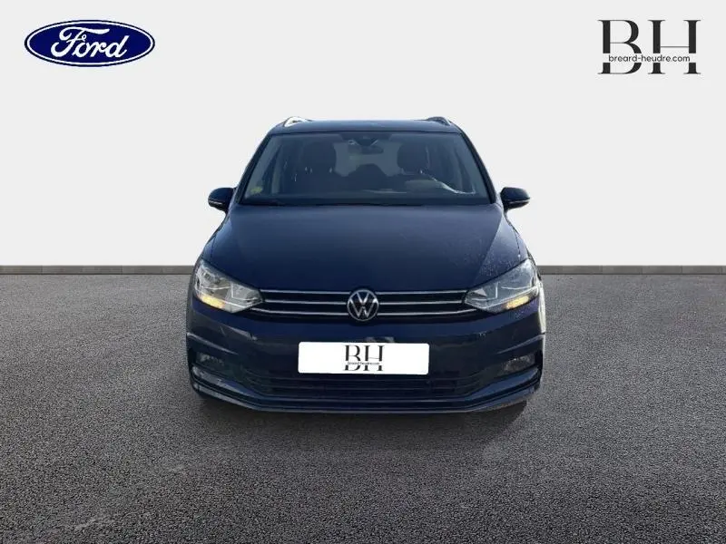 Vue avant d'un Volkswagen Touran bleu Atlantique métallisé avec calandre chromée et feux allumés.