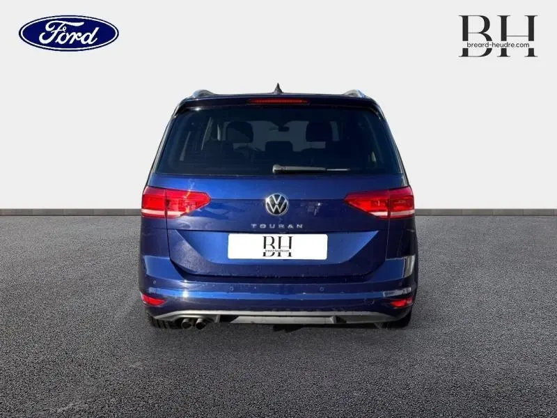 Vue arrière d'un Volkswagen Touran bleu Atlantique métallisé avec feux rouges et double sortie d'échappement visible.