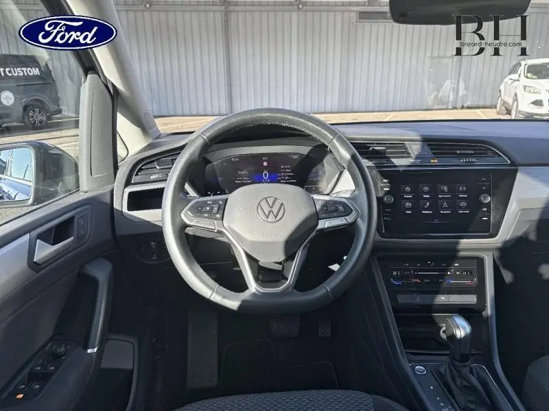Vue intérieure centrée sur le volant cuir multifonction d'un Volkswagen Touran 2023, avec tableau de bord digital et écran tactile.