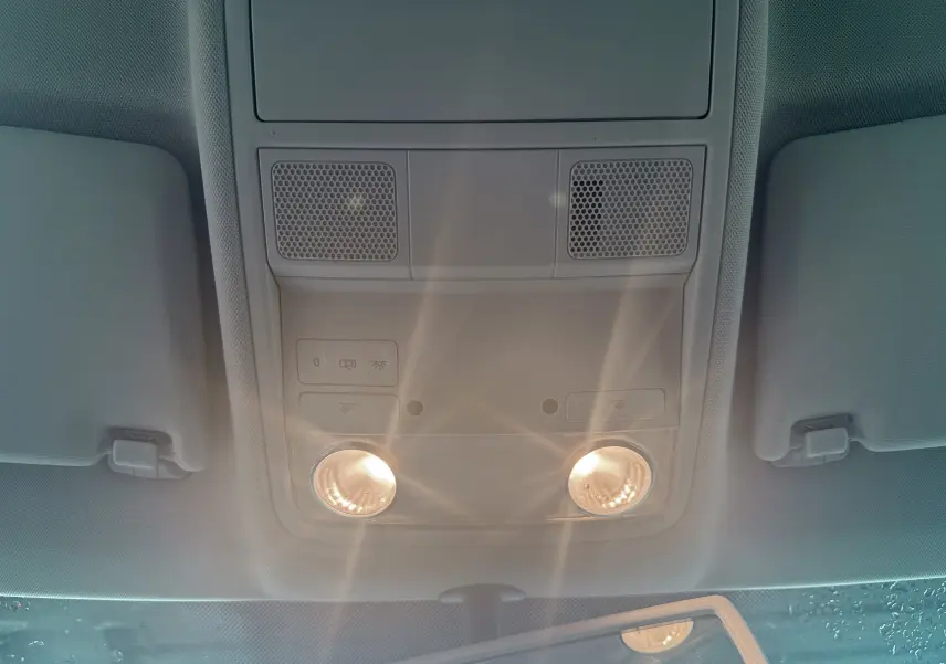 Plafonnier intérieur allumé vu de dessous dans un Volkswagen Tiguan blanc, avec pare-soleil et rétroviseur partiellement visible.