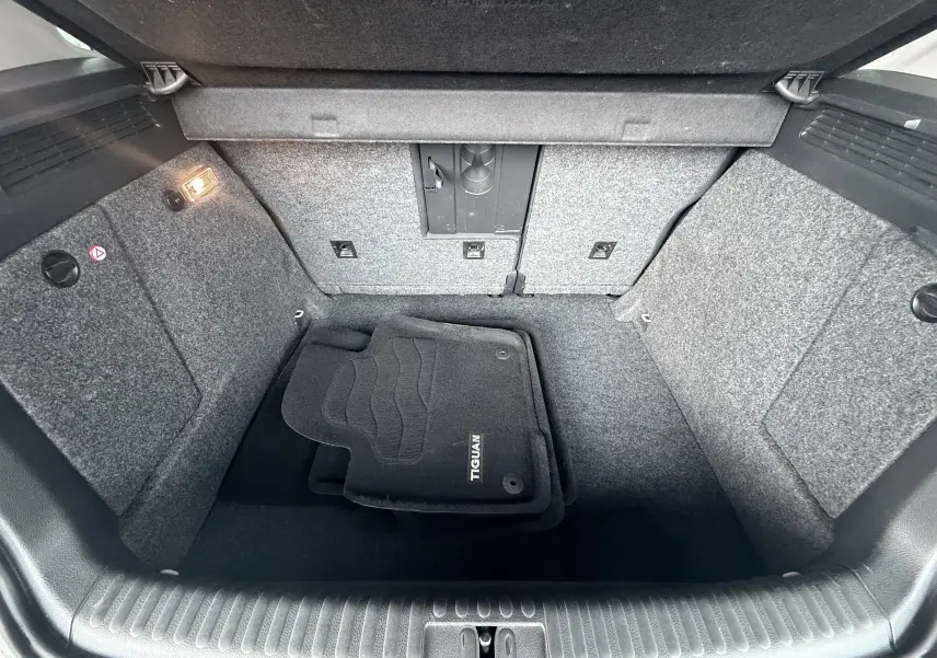 Vue intérieure du coffre gris foncé du Volkswagen Tiguan 2.0 TDI 140 de 2010 avec tapis de sol noirs marqués Tiguan.