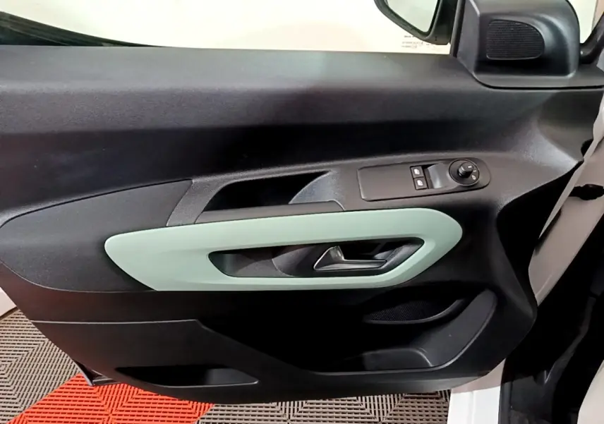 Vue intérieure côté gauche de la porte avant d'un Citroën Berlingo blanc, avec poignée vert clair et commandes électriques.
