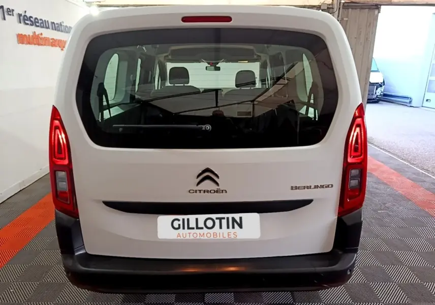 Vue arrière d'un Citroën Berlingo blanc XL, avec feux arrière allumés et vitre arrière large visible en intérieur.