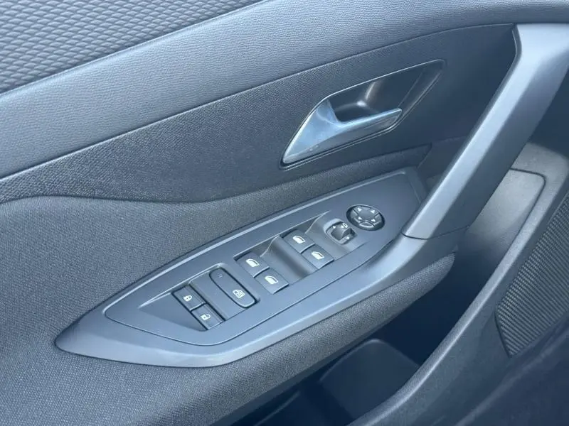 Vue rapprochée de la porte avant gauche de la Peugeot 308 2025, montrant les commandes électriques des vitres et rétroviseurs.