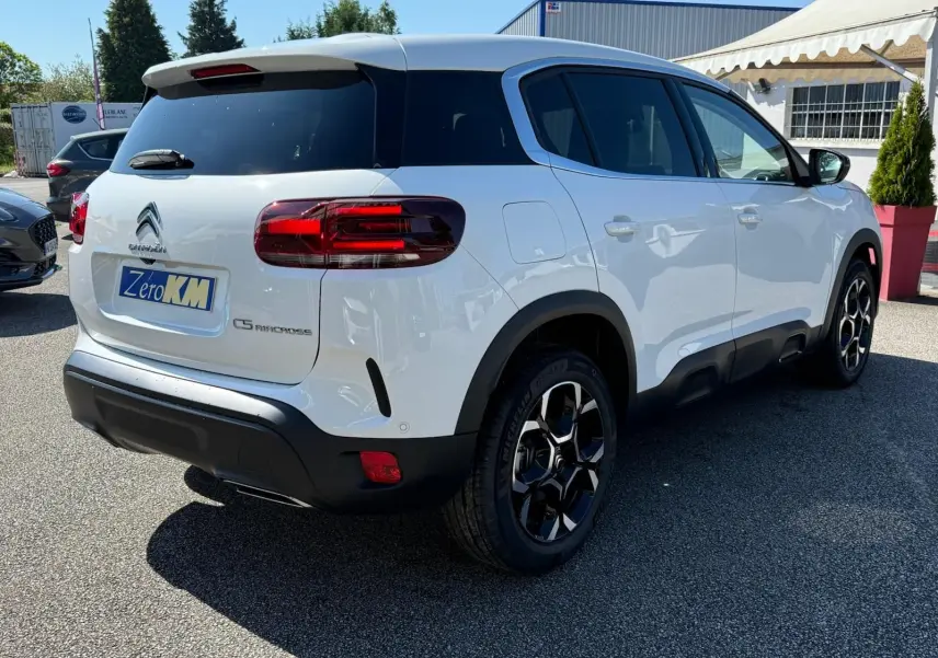 Vue 3/4 arrière droite d'un Citroën C5 Aircross blanc banquise avec jantes bi-ton et protections noires basses.