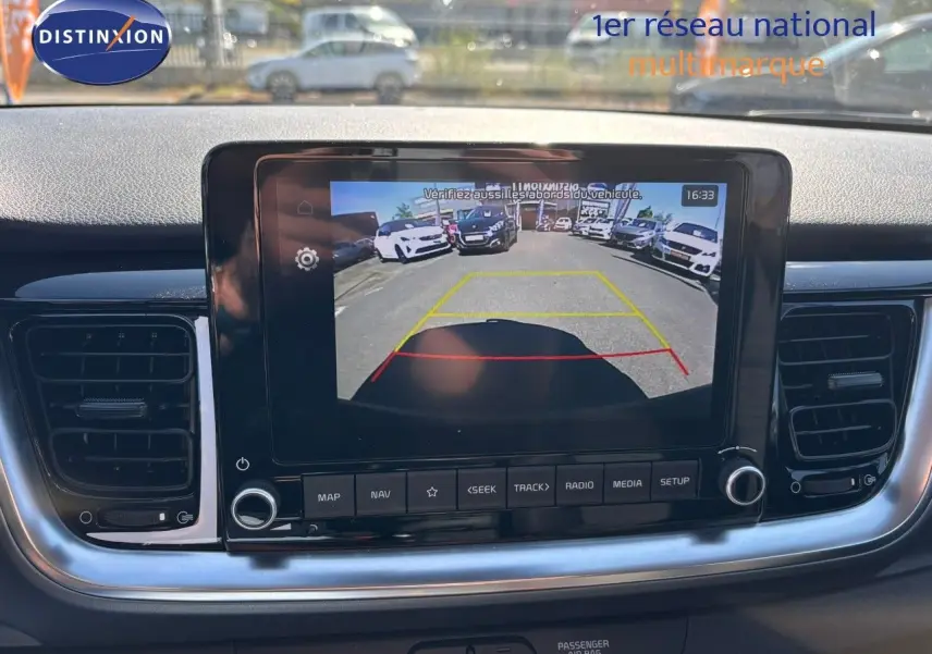 Écran central du tableau de bord du Kia Stonic 2024 montrant la caméra de recul avec vue arrière sur parking.