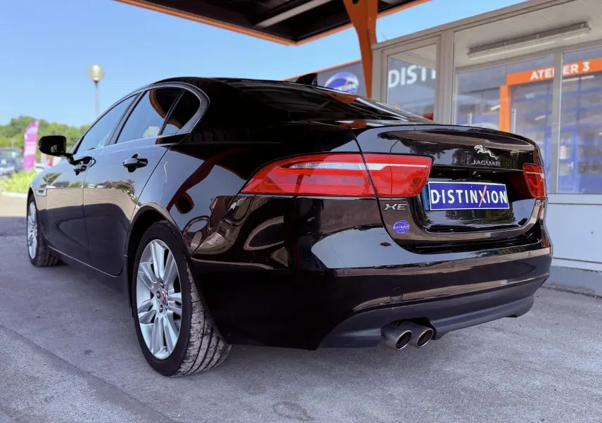Vue 3/4 arrière gauche d'une Jaguar XE noire brillante avec double sortie d'échappement et feux arrière rouges.