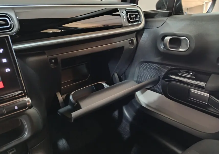 Intérieur côté passager de la Citroën C3 gris foncé 2024, boîte à gants ouverte et tableau de bord noir brillant.