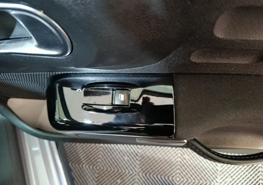 Gros plan sur la commande de lève-vitre côté conducteur d'une Citroën C3 gris foncé, avec poignée de porte visible.