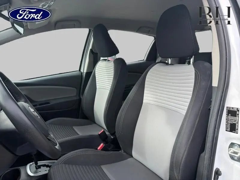 Vue intérieure côté conducteur montrant les sièges avant bicolores noir et gris d'une Toyota Yaris blanche.