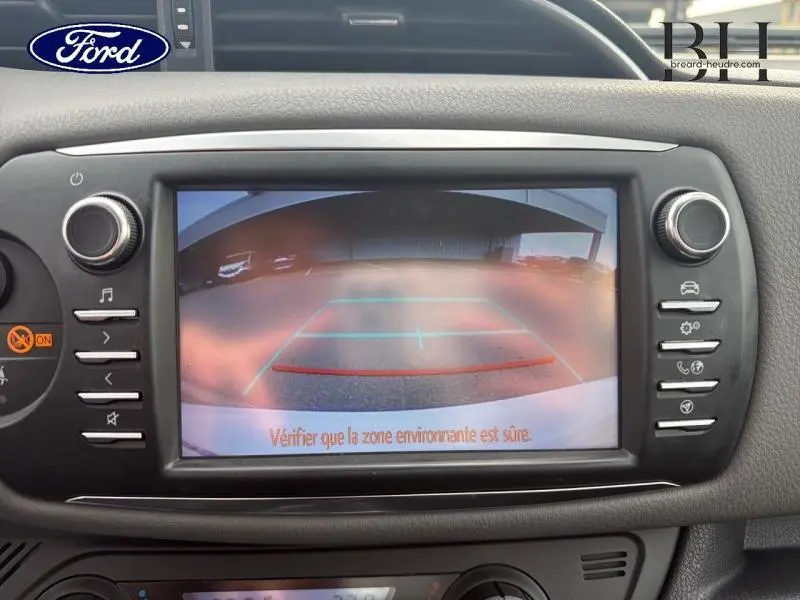 Image de l'écran de caméra de recul d'une Toyota Yaris 116h France Business blanche, affichant la zone arrière avec repères de guidage.