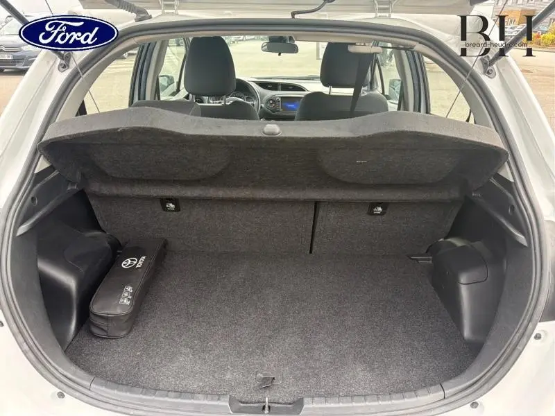 Vue arrière du coffre ouvert d'une Toyota Yaris 116h blanc pur, avec tablette cache-bagages et intérieur tissu noir visible.
