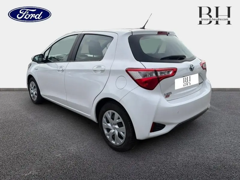 Vue 3/4 arrière droite d'une Toyota Yaris 116h France Business blanche avec feux arrière LED et jantes enjoliveurs.
