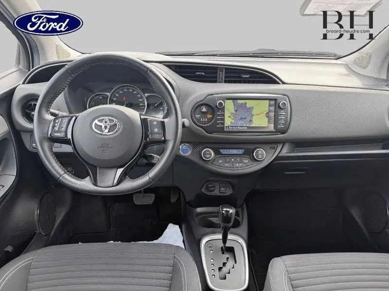 Vue intérieure avant de la Toyota Yaris 116h blanche, tableau de bord avec écran tactile et volant multifonction cuir.
