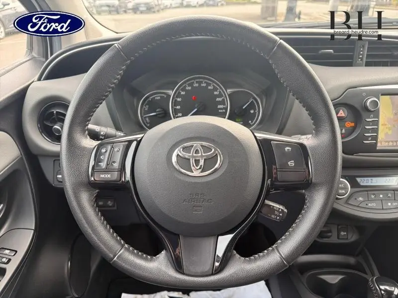 Vue rapprochée du volant cuir multifonction noir d'une Toyota Yaris 116h 2020 avec tableau de bord et écran tactile visibles.