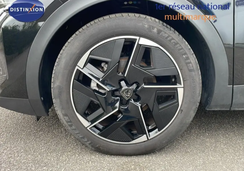 Gros plan sur la roue avant droite noire métal d'une Peugeot 408 Hybrid 145ch avec jante au design moderne bicolore.