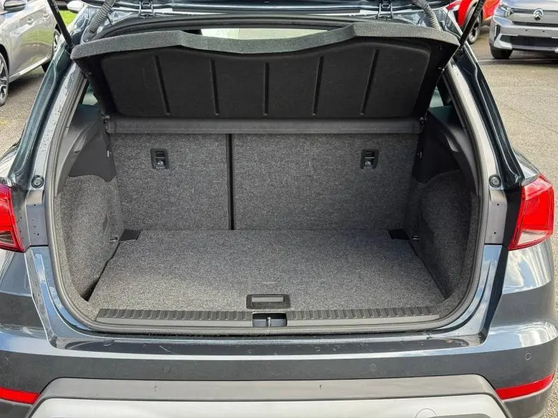 Coffre ouvert vu de l'arrière d'un SEAT Arona 2025 bleu Saphir Métal avec toit blanc, montrant l'espace de chargement vide.