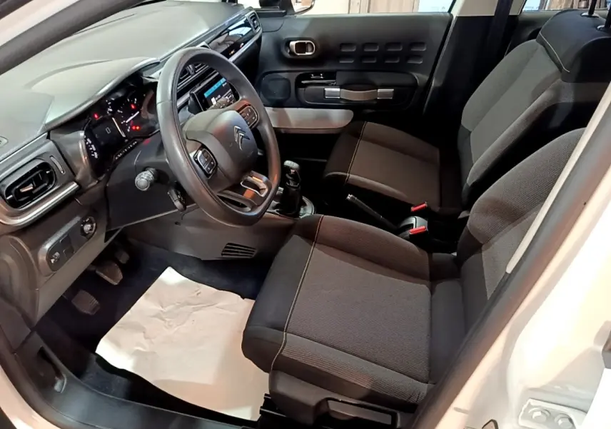 Vue intérieure côté conducteur de la Citroën C3 blanche 2020, montrant sièges tissu gris et tableau de bord moderne.