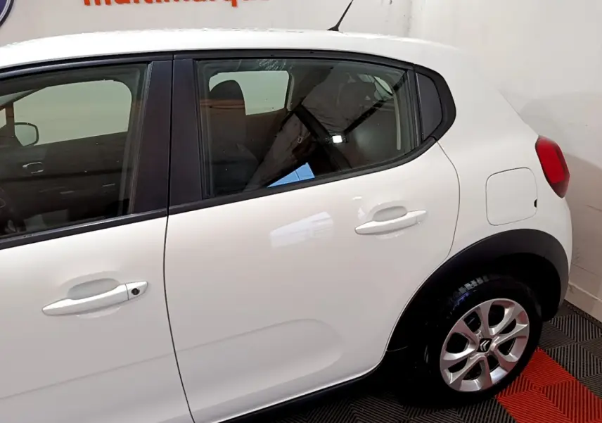 Vue latérale droite d'une Citroën C3 blanche avec poignées et rétroviseurs ton caisse, en intérieur showroom.