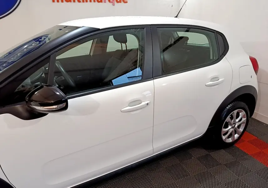 Vue latérale droite d'une Citroën C3 blanche avec rétroviseur noir brillant et jantes alliage en intérieur showroom.